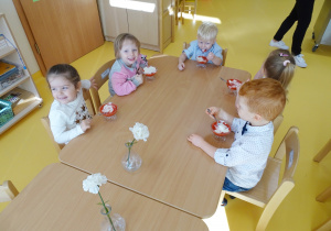 Zadowolone dzieci jedzą biało - czerwony poczęstunek.